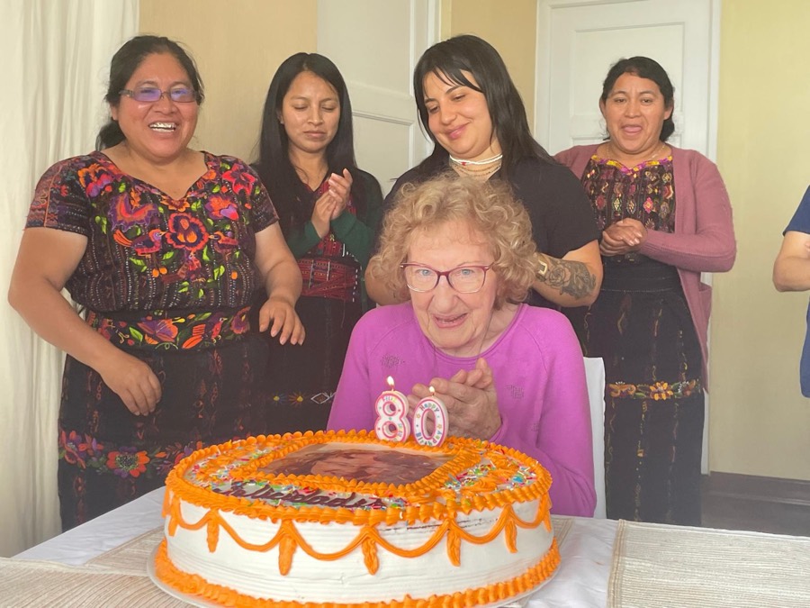 Denise Rauber feiert ihren 80. Geburtstag vor einer grossen Torte, umgeben vom lachenden PAZ MUNDO Team