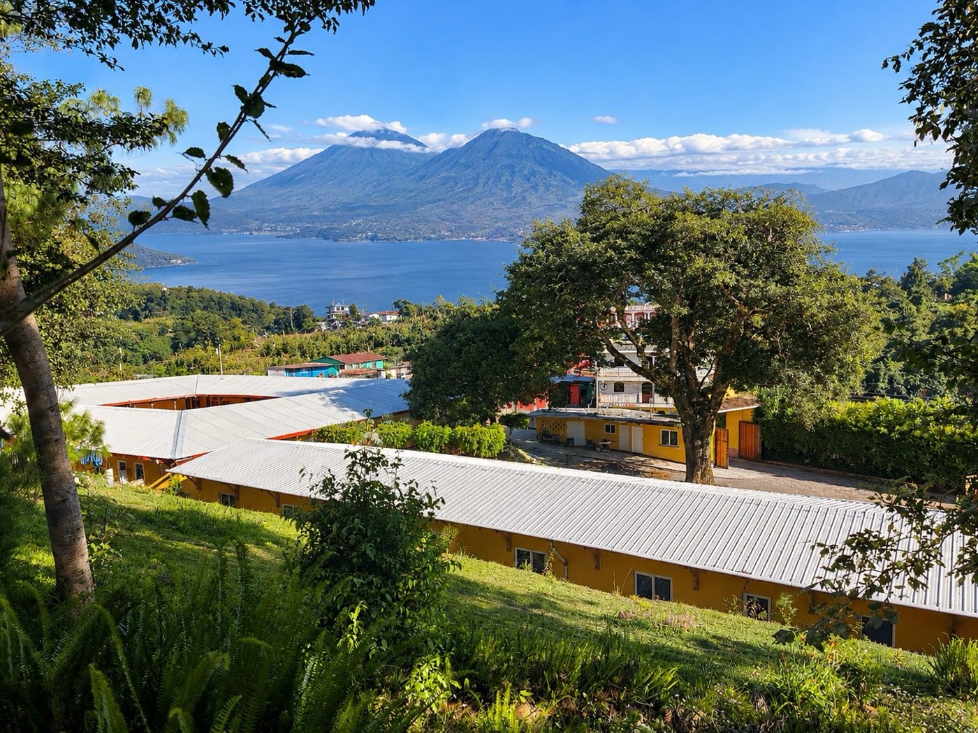 L’Hôpital PAZ MUNDO avec ses bâtiments jaunes sur la pente, derrière le lac Atitlán et les volcans, représentation générée par IA