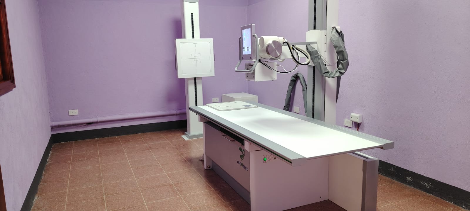 Der neue Röntgenraum im Hospital PAZ MUNDO mit Röntgentisch und Wandstativ vor lila Wänden